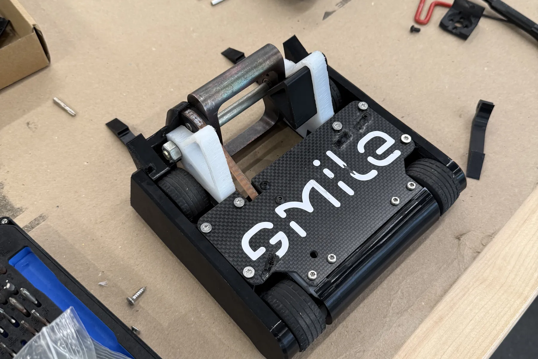 Carbon-fiber 3lb combat robot lettered Smile, on a workbench during assembly